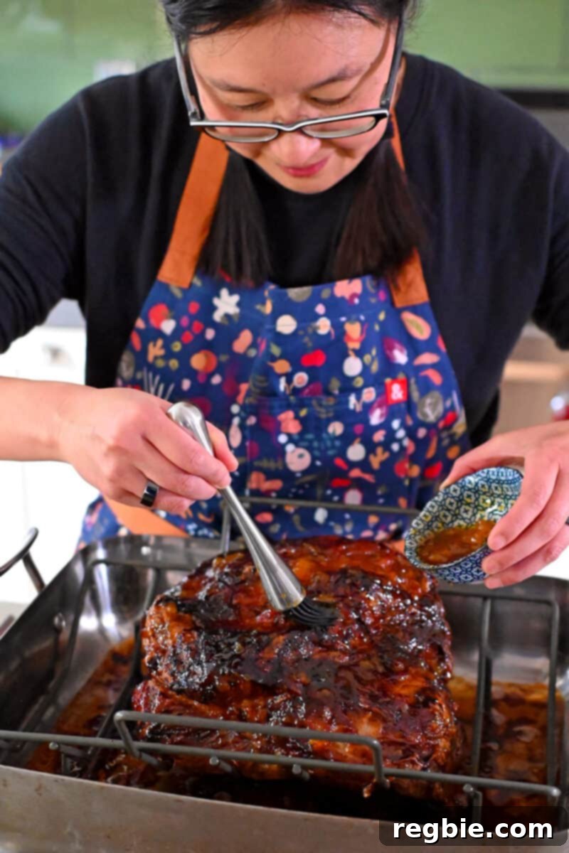Effortless Peach Glazed Pork Roast 14 An Asian woman is brushing peach jam glaze on a cooked pork shoulder roast.