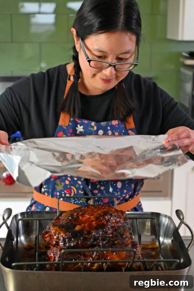 Effortless Peach Glazed Pork Roast 15 An Asian woman in glasses is placing a large piece of aluminum foil on top of the slow roasted pork shoulder.