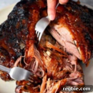 Two forks are shredding a pork shoulder roast that is topped with a peach barbecue sauce.