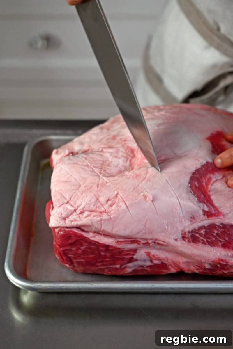 Effortless Peach Glazed Pork Roast 4 A chef's knife is cutting a shallow crosshatch pattern in the fat cap on top of a bone-in pork shoulder roast.