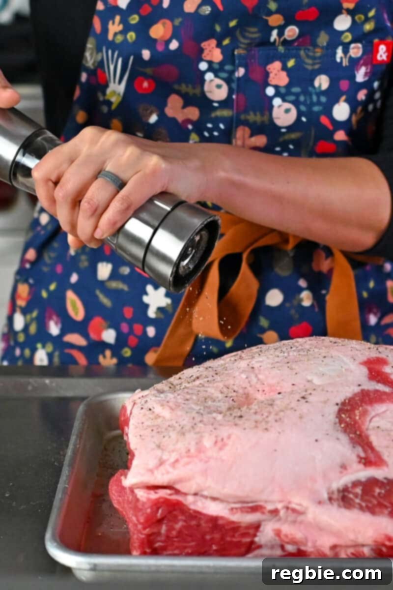 Effortless Peach Glazed Pork Roast 6 A person is using pepper mill to add fresh cracked black pepper on a large pork shoulder roast.