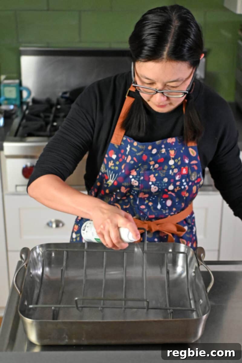 Effortless Peach Glazed Pork Roast 7 An Asian woman in glasses is spraying avocado oil on a rack in a roasting pan.