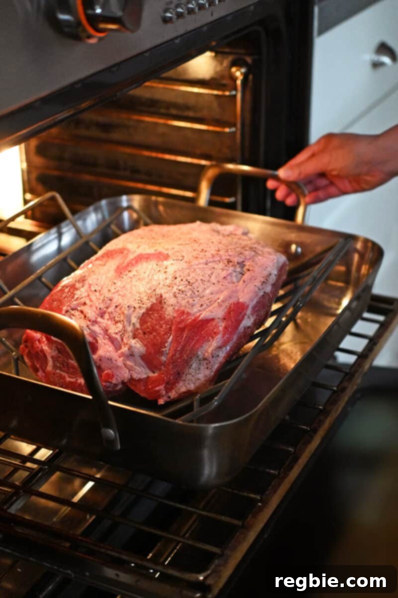 Effortless Peach Glazed Pork Roast 10 Placing a roasting pan with a seasoned bone-in pork shoulder roast into an open oven.