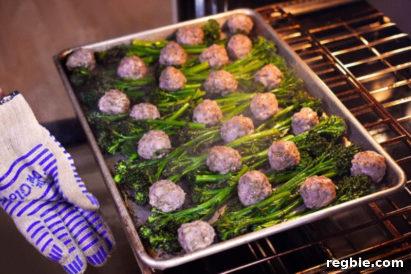 An overhead shot of someone rotating a tray of Sheet Pan Meatballs and Broccolini at the halfway point of cooking to ensure even browning.