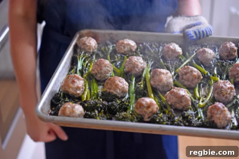 Someone carrying a steaming tray of Sheet Pan Meatballs and Broccolini freshly removed from the oven, ready to be served.