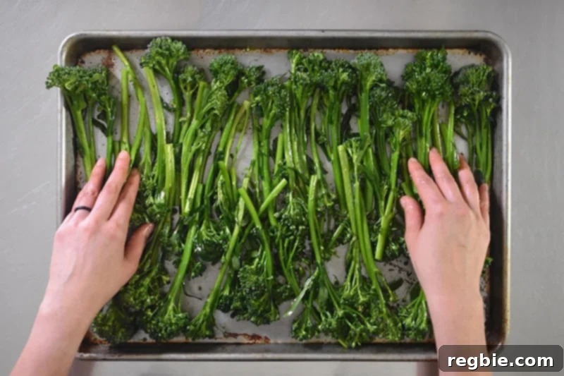 Overhead shot of seasoned broccolini neatly arranged in a single layer on a rimmed baking sheet, ready for the oven.