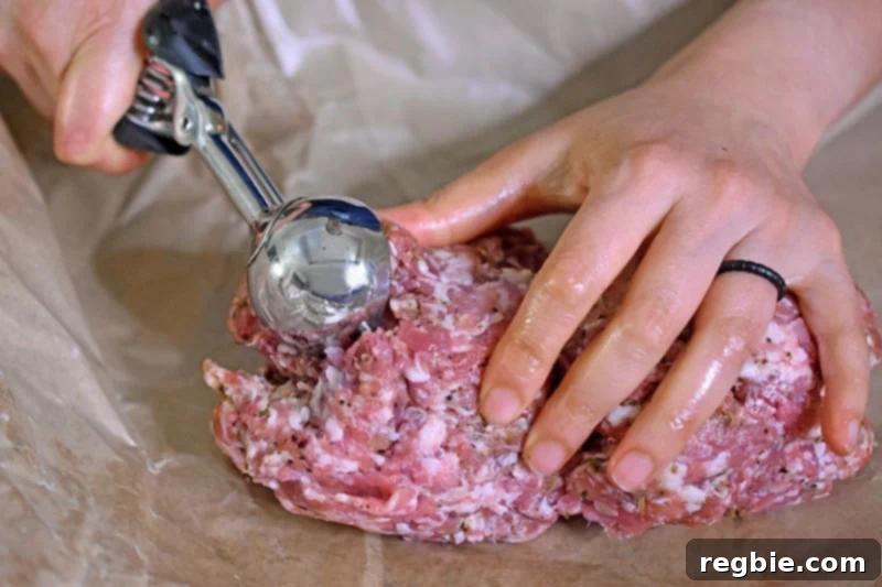 Two hands are shown scooping bulk Italian sausage with a medium-sized disher, preparing to form meatballs.