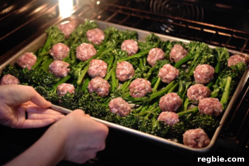 Two hands are placing a tray of Sheet Pan Meatballs and Broccolini into the oven, signaling the start of the roasting process.