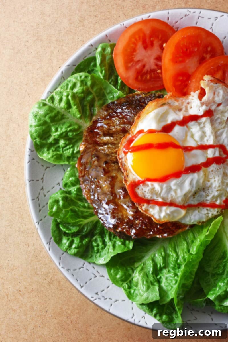 An overhead shot of a Nomster Burger on a bed of lettuce and topped with a crispy fried egg, sriracha, and sliced tomatoes, showcasing a vibrant, healthy meal.