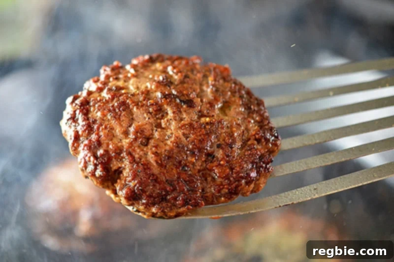 A perfectly cooked Nomster burger, with a golden crust, is being lifted out of a cast iron skillet with a metal fish spatula.