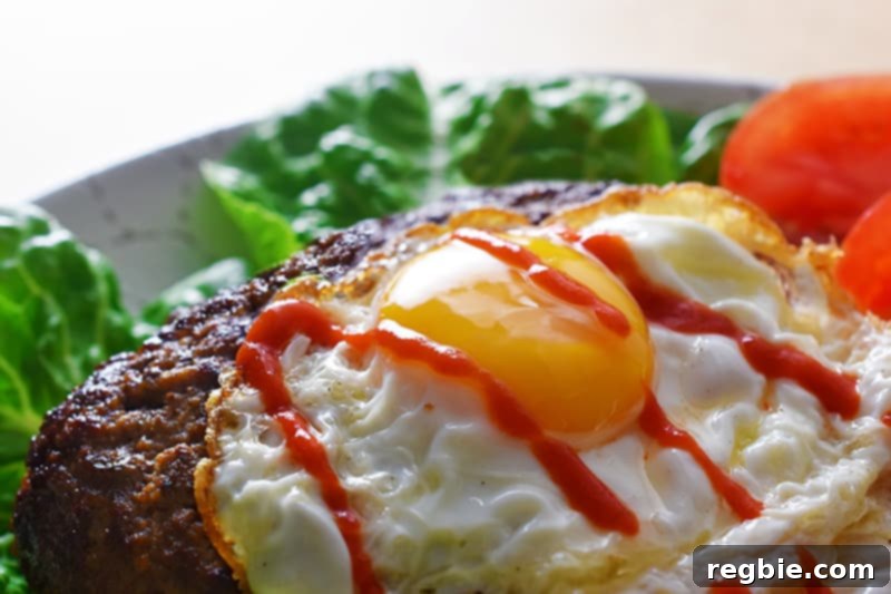 A side view of a beautifully assembled Nomster burger, presented on a bed of fresh lettuce, topped with a crispy sunny-side-up egg, and a delicious drizzle of sriracha.
