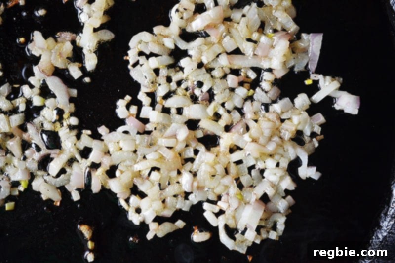 Overhead shot of finely diced shallots sautéing in a cast iron skillet, turning golden and aromatic.