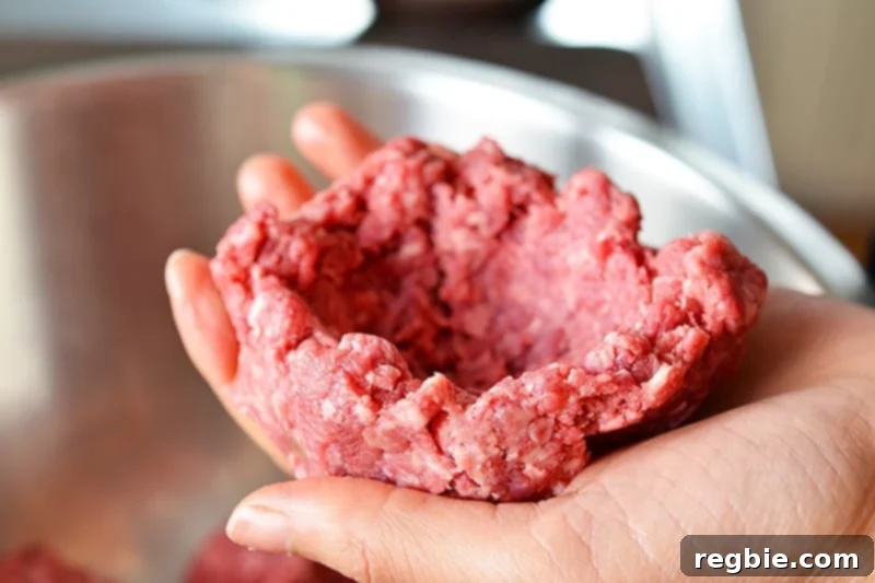 A hand holding a portion of raw ground beef, carefully formed into a bowl shape to prepare for stuffing.