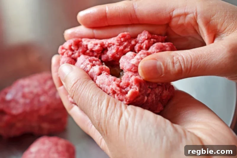 Two hands are carefully sealing up the ground beef around the cooked shallots to form a perfectly shaped ball.