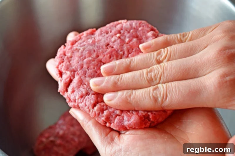 Two hands gently patting a Nomster burger flat, creating a uniform, shallot-stuffed patty ready for frying.
