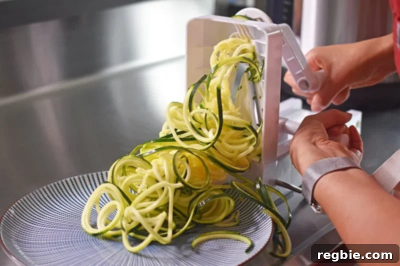 A close-up shot of hands actively using a spiralizer to create fresh zucchini noodles, highlighting the ease of making homemade veggie pasta.