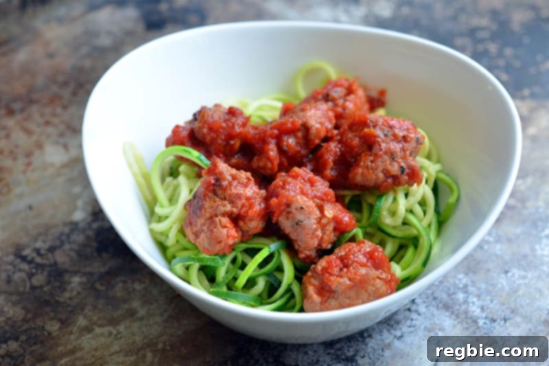 A white bowl featuring a classic serving of tender meatballs nestled in rich sauce, accompanied by fresh zucchini noodles.