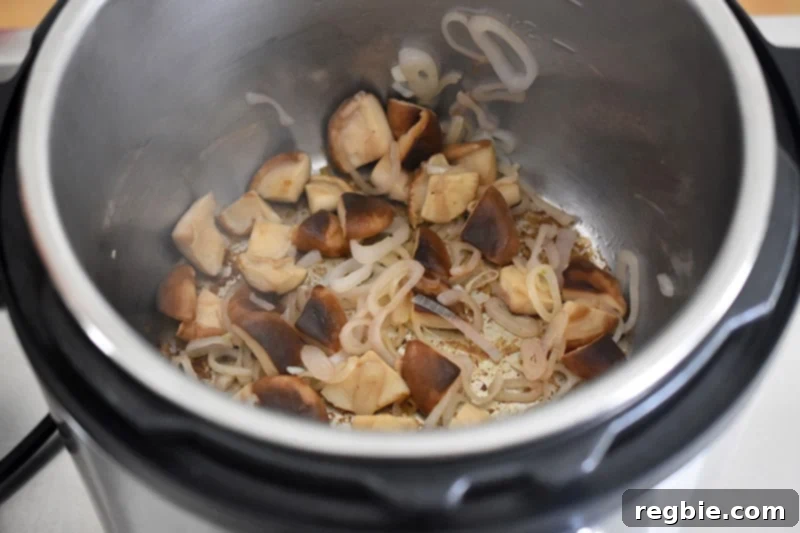 An overhead shot showing cooked, softened shallots and tender shiitake mushrooms in an open Instant Pot.