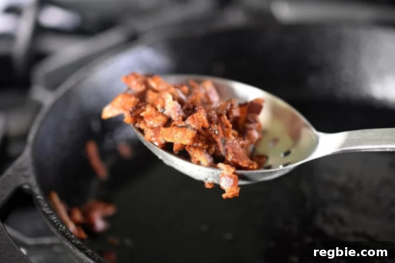 Crispy Bacon Brussels Sprouts 6 Removing crispy bacon bits from a cast iron skillet with a slotted spoon, reserving the flavorful bacon grease.