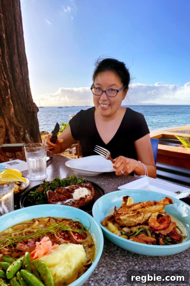 A smiling Asian woman is eating a gluten-free dinner by the beach in Maui