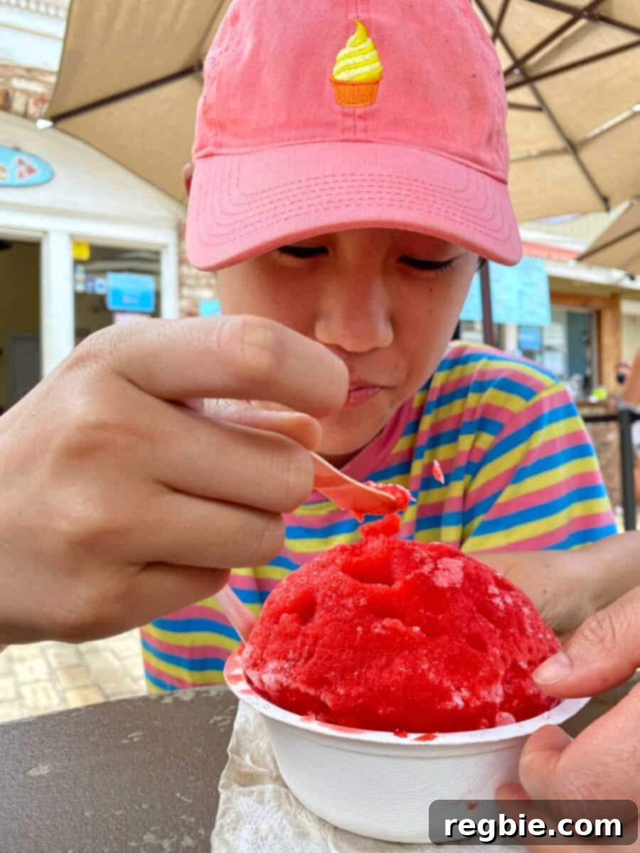 A boy in a pink hat is eating shave ice from Ululani's in Maui