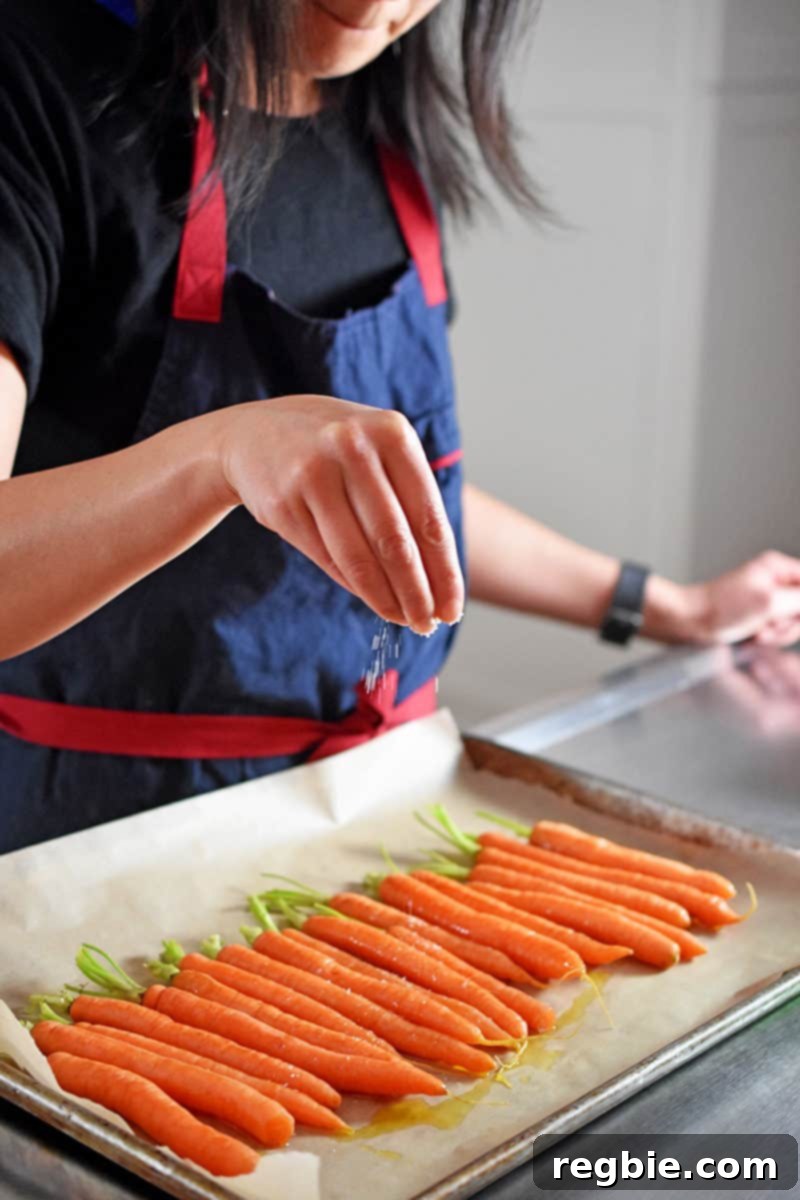Simple Whole30 Roasted Vegetable Creations 7 A black haired woman is sprinkling salt on a tray of carrots.