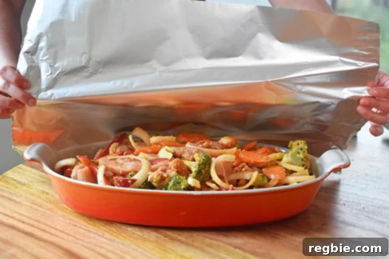 A large piece of aluminum foil is carefully placed and sealed over the top of the casserole dish, preparing it for baking.
