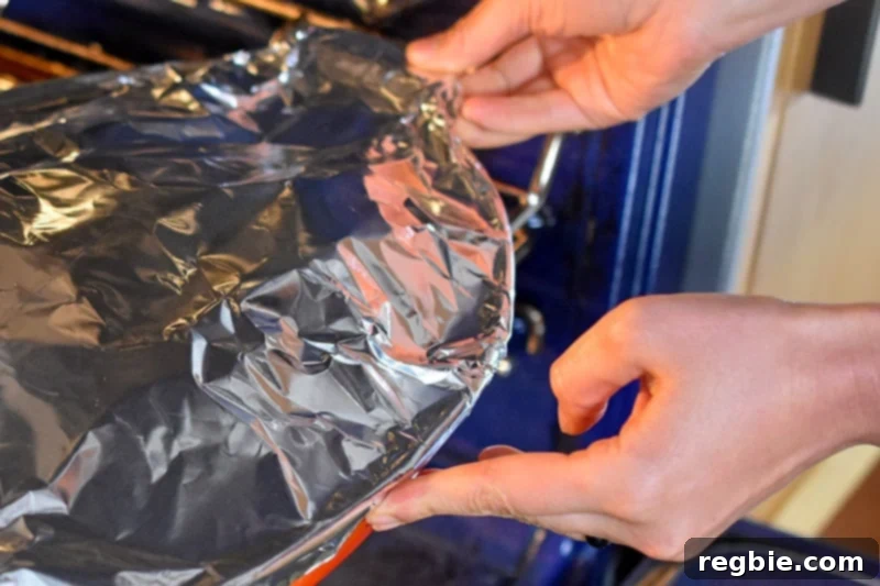 The foil-covered Thai Chicken Curry Casserole dish is being carefully placed into a preheated oven for baking.