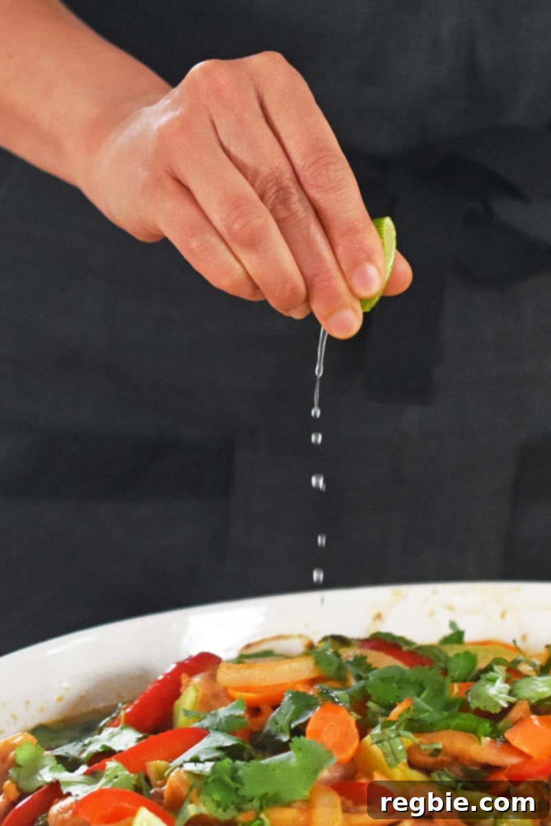 A hand squeezing fresh lime juice over the freshly baked Thai Chicken Curry Casserole, adding a bright, zesty finish to the dish.