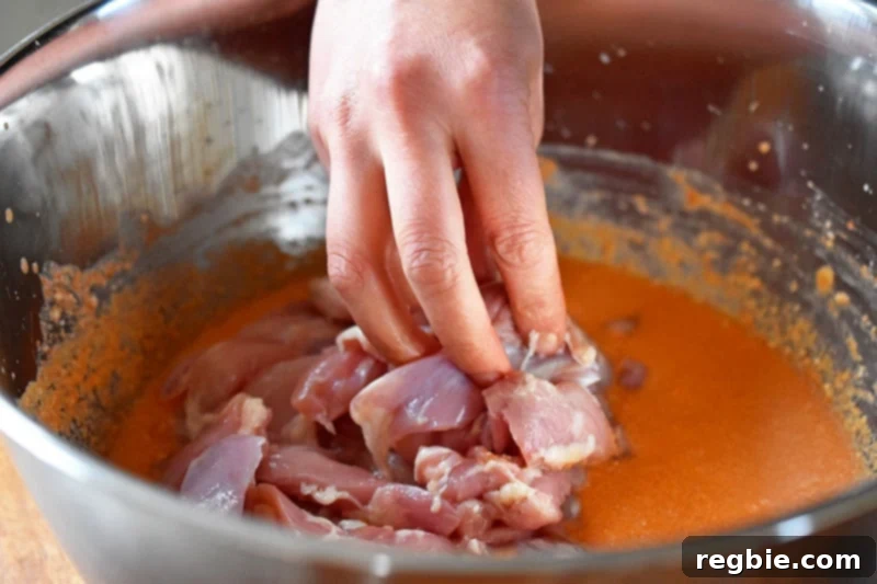 Thinly sliced boneless, skinless chicken thighs being added to the prepared curry sauce in a large metal mixing bowl.