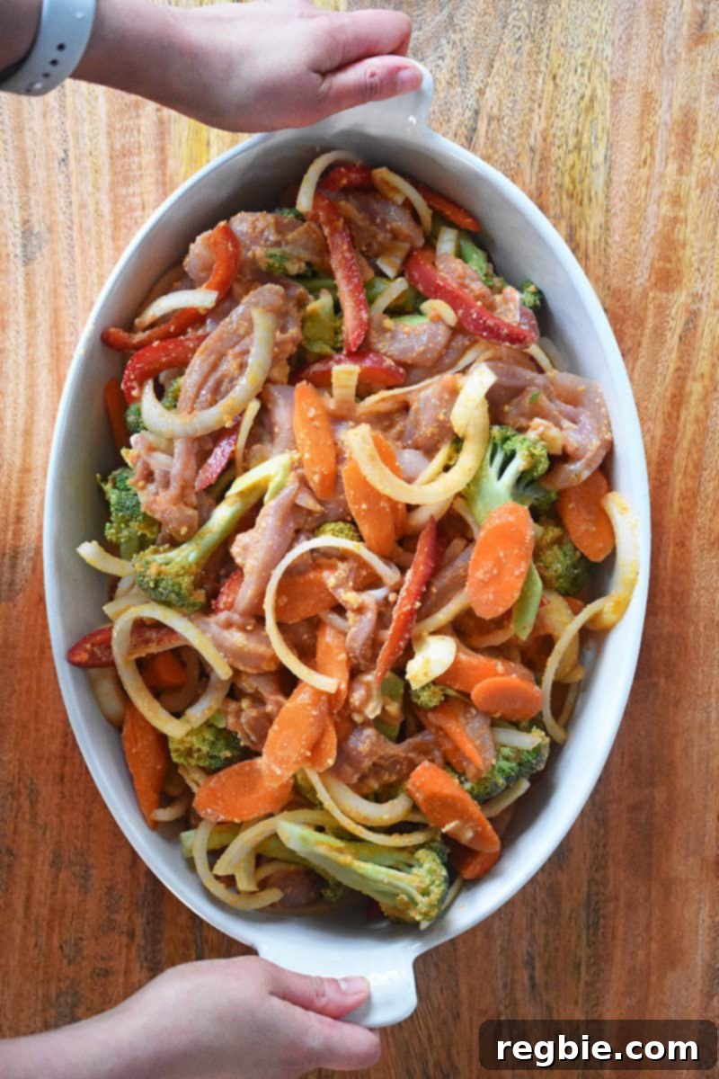 An overhead shot of the mixed Thai Chicken Curry Casserole ingredients, including chicken and colorful vegetables in a rich sauce, arranged evenly in a 9x13 inch casserole dish, ready for baking.