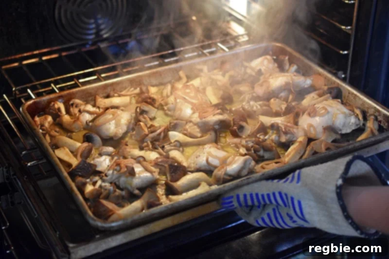 A steaming sheet pan of chicken and mushrooms being rotated midway through the cooking process for even roasting.