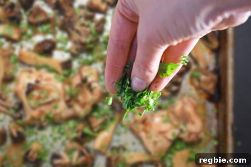 Freshly chopped green herbs, like parsley and chives, being sprinkled over the hot Sheet Pan Chicken and Mushrooms dinner.