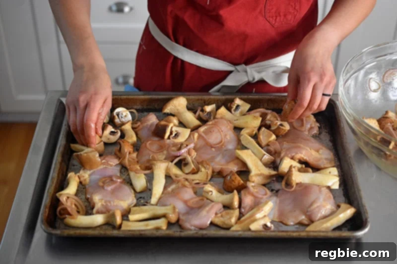 Arranging marinated mushrooms around the chicken thighs on the baking sheet to ensure even cooking.