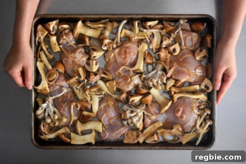 The final arrangement of chicken, mushrooms, and shallots in a single layer on the sheet pan before going into the oven.