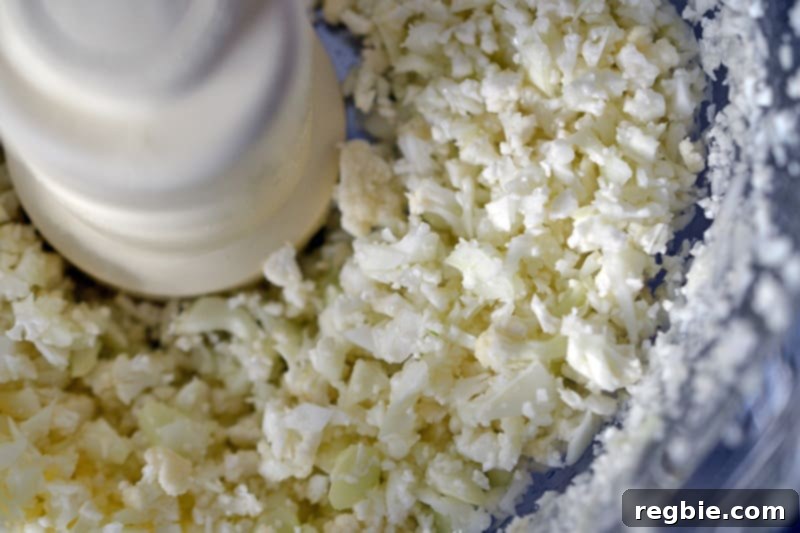 Easy Whole30 Paleo Keto Meatloaf Nut and Dairy Free 4 An overhead shot of fresh cauliflower florets being riced in a food processor, highlighting the process of creating a healthy, low-carb meatloaf filler.