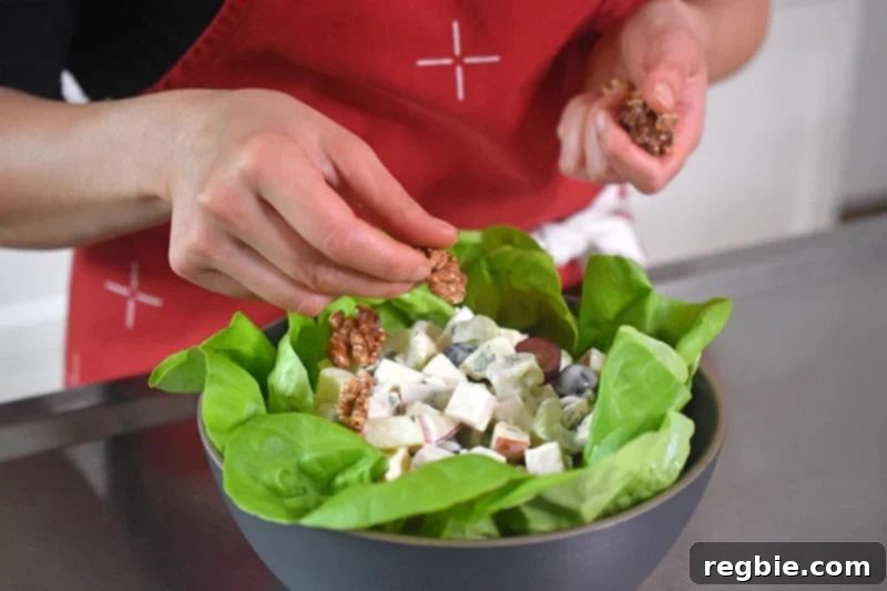 Toasted walnuts being carefully scattered over the top of a finished chicken Waldorf salad, adding the final crunchy garnish.