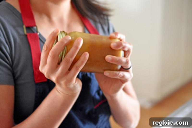 Shaking a jar of Nom Nom Paleo All-Purpose Stir-Fry Sauce, a key ingredient for quick and healthy Whole30 meals.