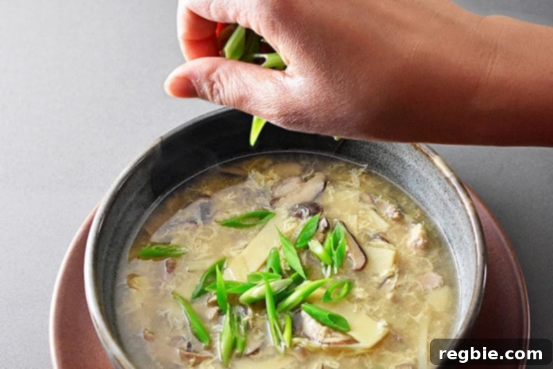 Zesty Whole30 Gluten Free Hot and Sour Soup 12 Garnishing a bowl of hot and sour soup with freshly sliced scallions, ready to be served.