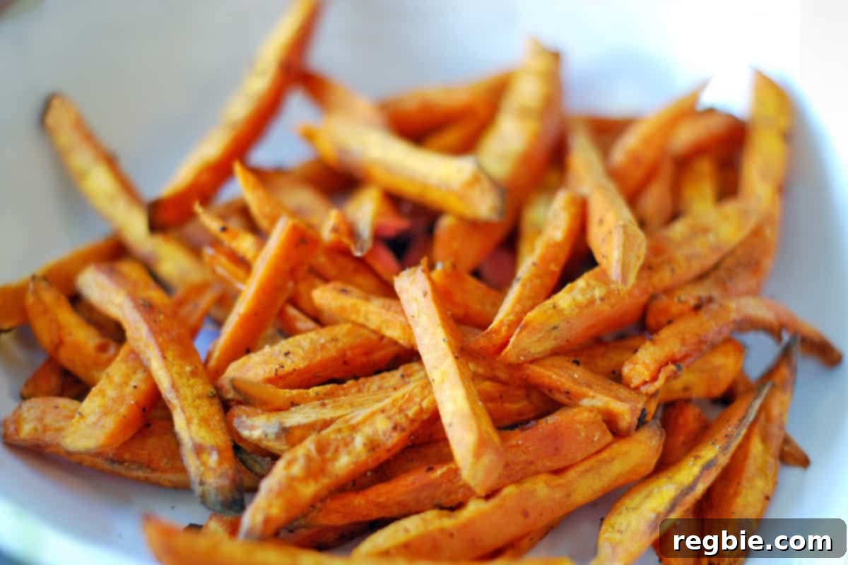 A close-up shot of a white ceramic bowl overflowing with perfectly golden and crispy sweet potato fries, ready to be enjoyed.