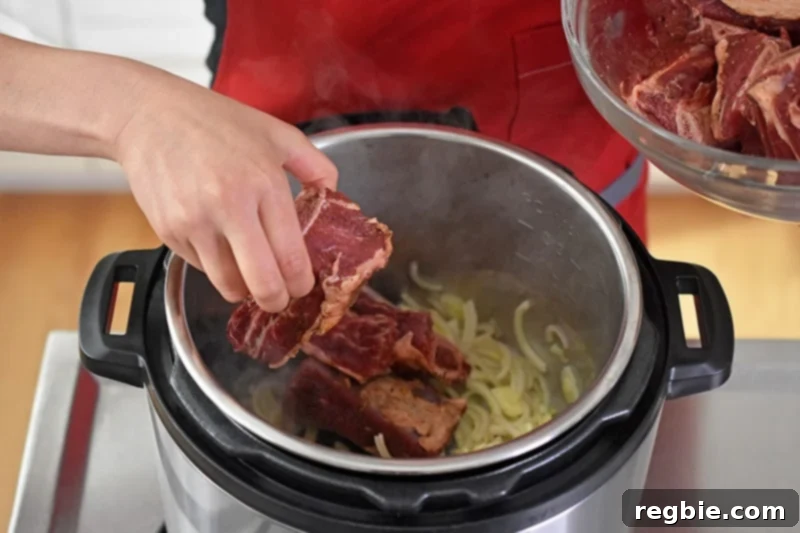 The seasoned short ribs are added to the Instant Pot filled with sliced shallots and garlic.