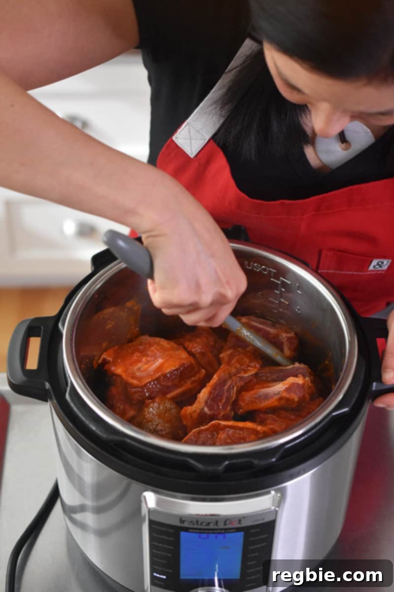 An overhead shot of someone stirring the Instant Pot Magic Short Ribs with a gray silicone spatula to combine all the ingredients thoroughly before cooking.