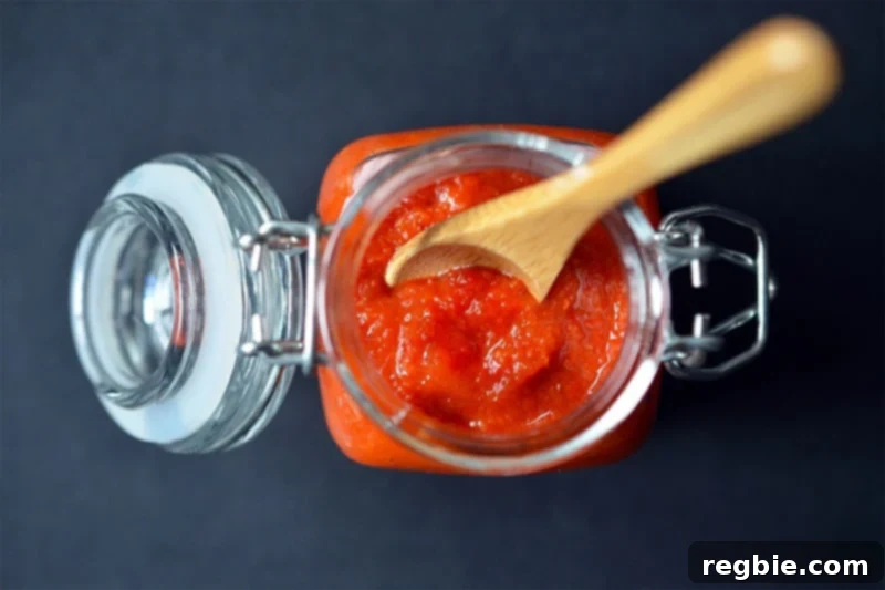 An overhead shot of a jar of Whole30 sriracha with a wooden spoon inside.