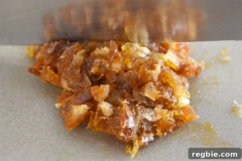 A close-up view of a chef's knife mincing Medjool dates on a gray cutting board to form a thick paste.