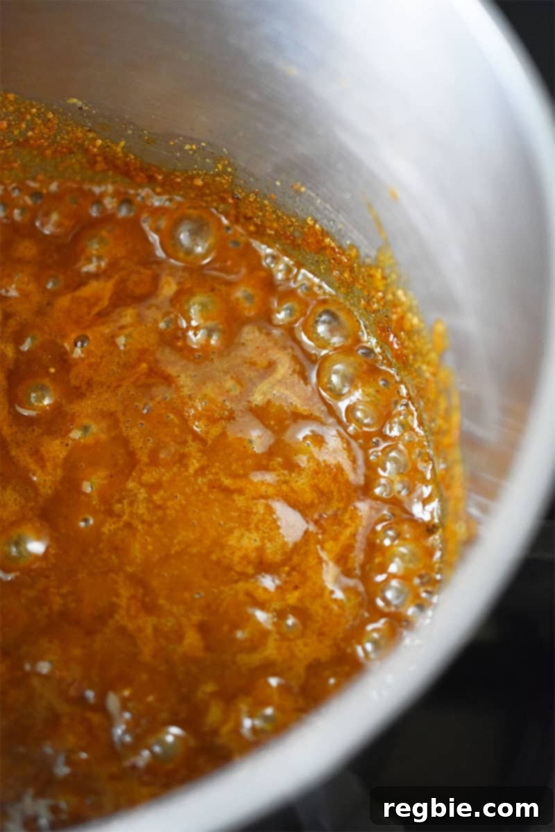 A close-up shot of the paleo hoisin sauce simmering gently in a small stainless steel saucepan, thickening and darkening.