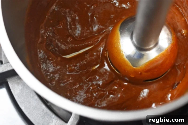 An immersion blender being used directly in the saucepan to make the paleo hoisin sauce extra smooth.
