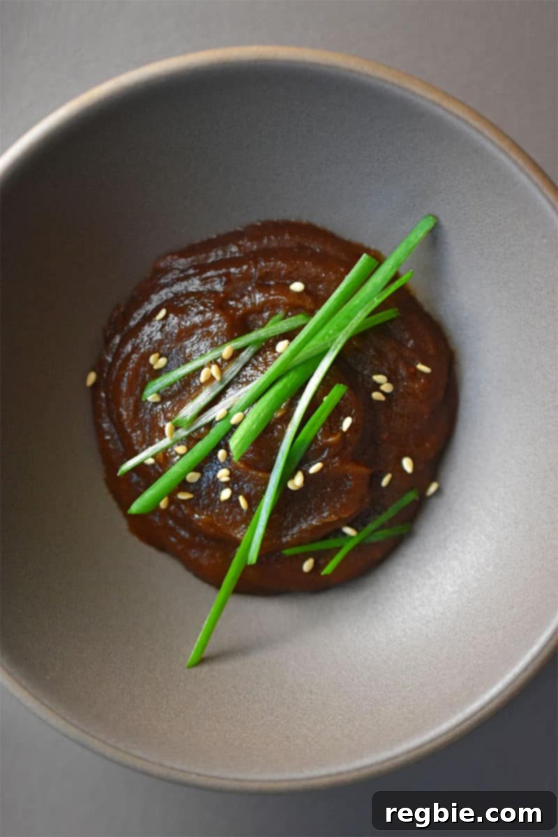 An overhead shot of the finished paleo hoisin sauce in a gray bowl, garnished with sesame seeds and chopped chives.
