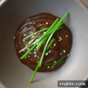 An overhead shot of a dish filled with paleo hoisin sauce topped with sesame seeds and chives