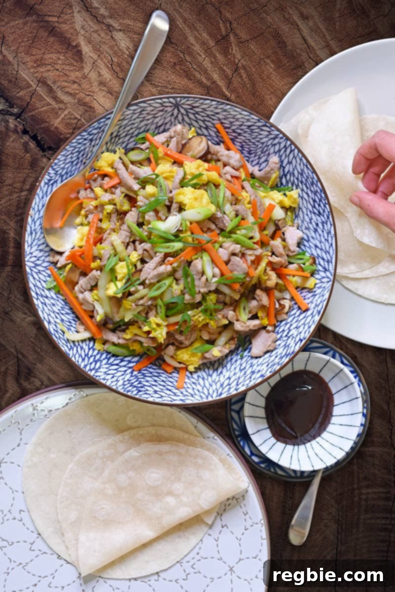 An overhead shot of a serving bowl filled with Paleo Moo Shu Pork, along with grain-free tortillas, and paleo hoisin sauce.