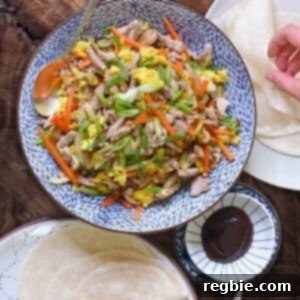 An overhead shot of a serving bowl filled with Paleo Moo Shu Pork, along with grain-free tortillas, and paleo hoisin sauce.
